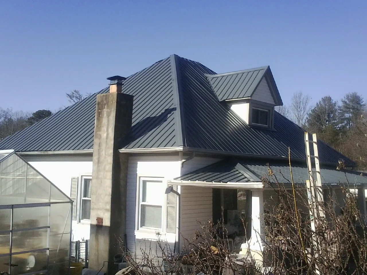 Dark blue standing seam metal roof on a white farmhouse with dormer — Slate & Tile Roof Repair by Roofing Brothers in Palacios