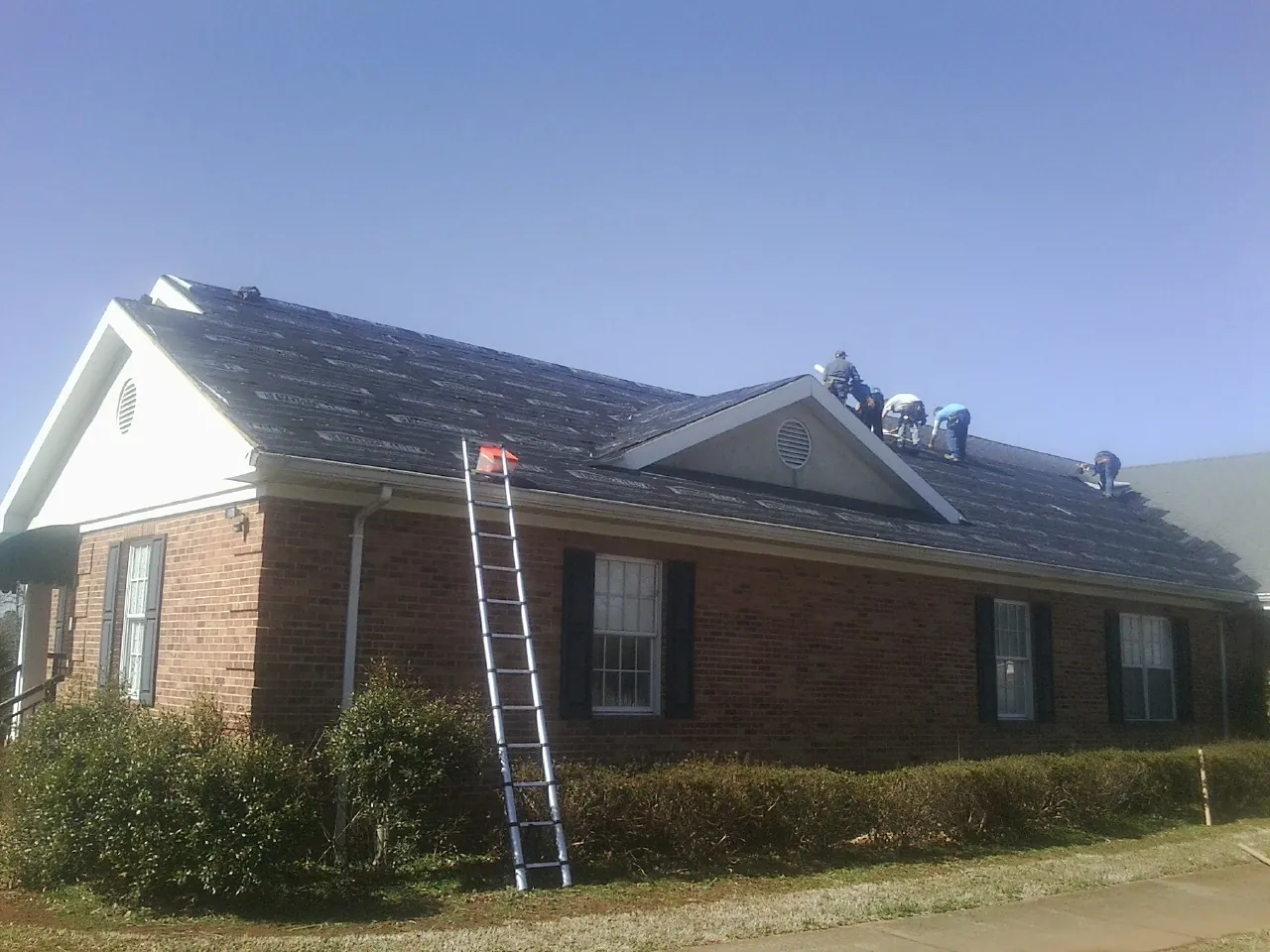 Crew tearing shingles off a brick ranch roof with a ladder set — Metal Roof Repair work by our crew in Palacios