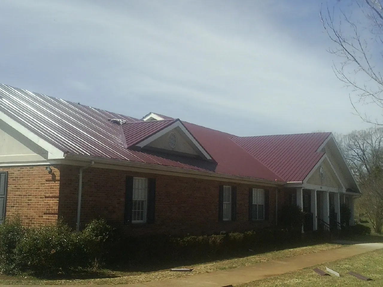Red metal roof with gabled entries on a long brick building, from a Hail Damage Roof Repair job in Palacios