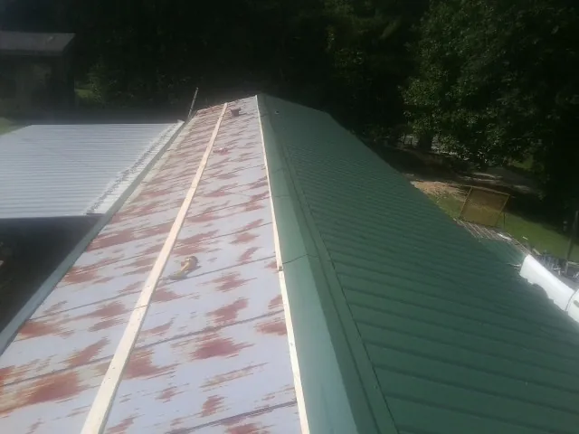 Old rusted panels beside newly installed green metal roofing — Wind Damage Roof Repair by Roofing Brothers in Palacios