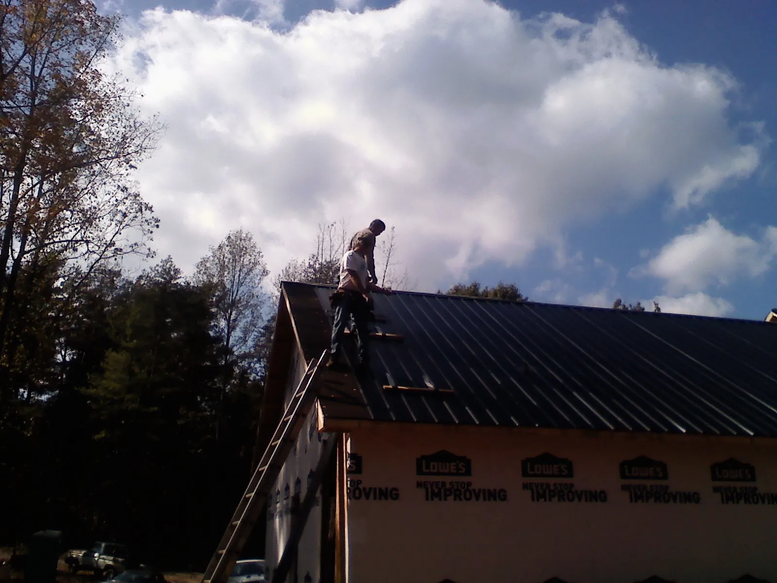 Roofer fastening dark metal panels high against a cloudy sky, from a Roof Inspection job in Palacios