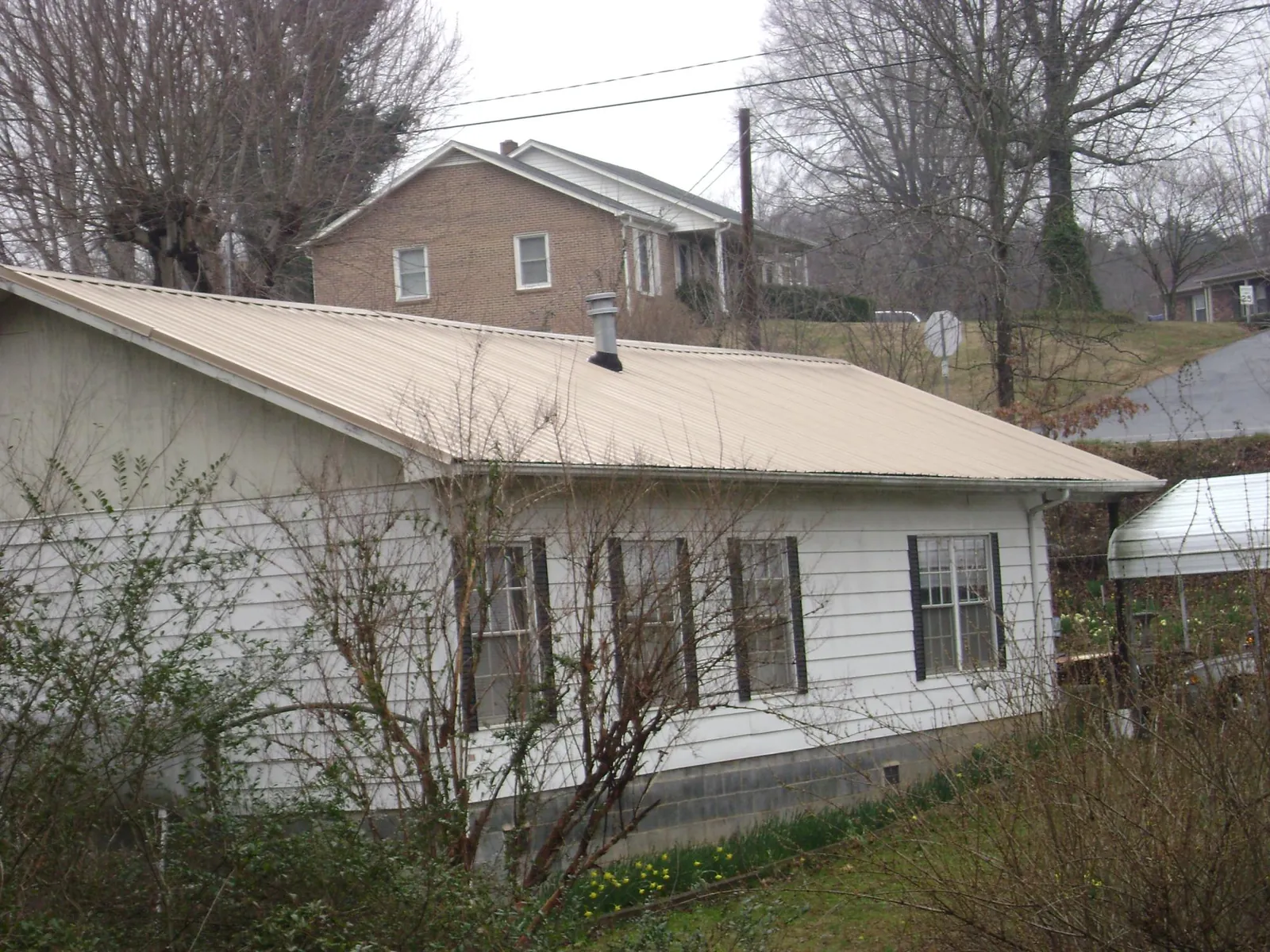 Tan metal roof on a white sided house set into a hillside — Commercial Roofing by Roofing Brothers in Palacios