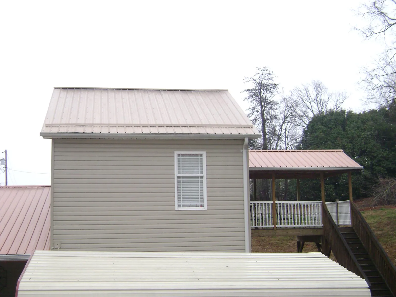 Tan metal roofs on a two story addition and attached porch, from a Roof Replacement job in Palacios